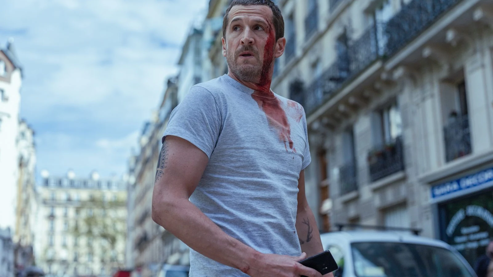 Guillaume Canet appears bloodied on a city street in an official Netflix press image.