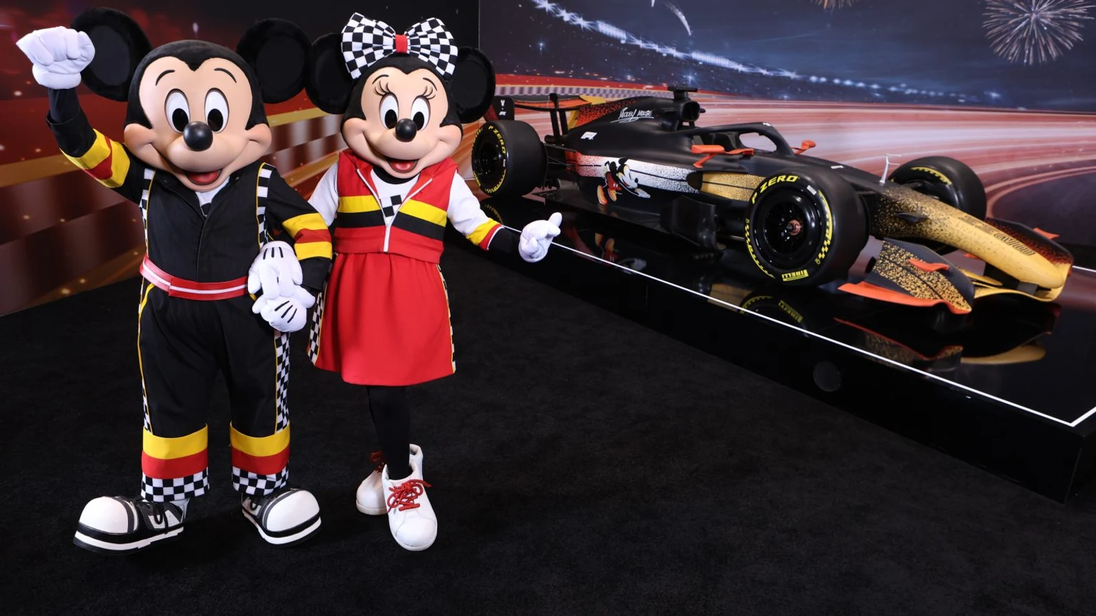 Mickey Mouse and Minnie Mouse in racing outfits beside a Formula 1 show car.