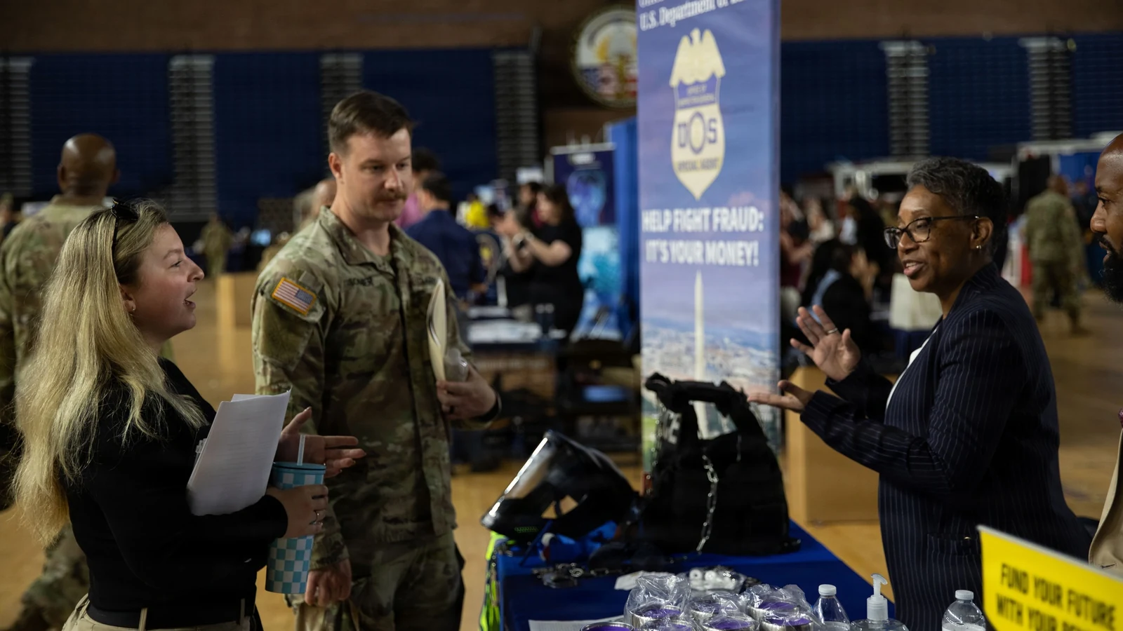 Job seekers talk with recruiters at tables inside a crowded career fair.