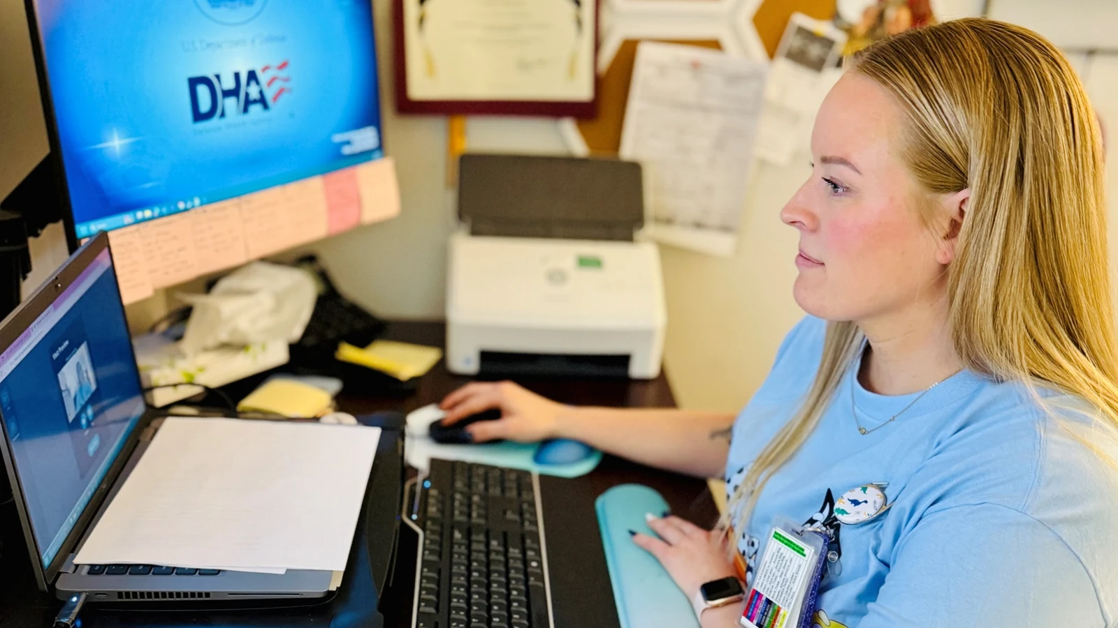 A nurse sits at a desk and signs into a virtual-care platform on a large monitor.