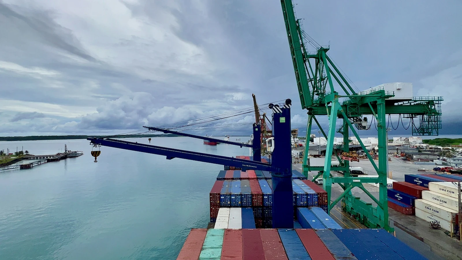 A container ship is worked by cranes at the Port of Guam beneath a broad evening sky.