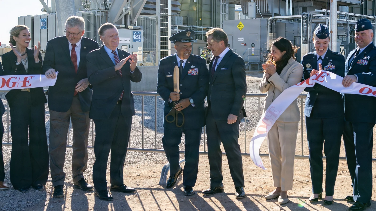Officials cut a ribbon in front of a natural-gas peaking plant and its turbine building.