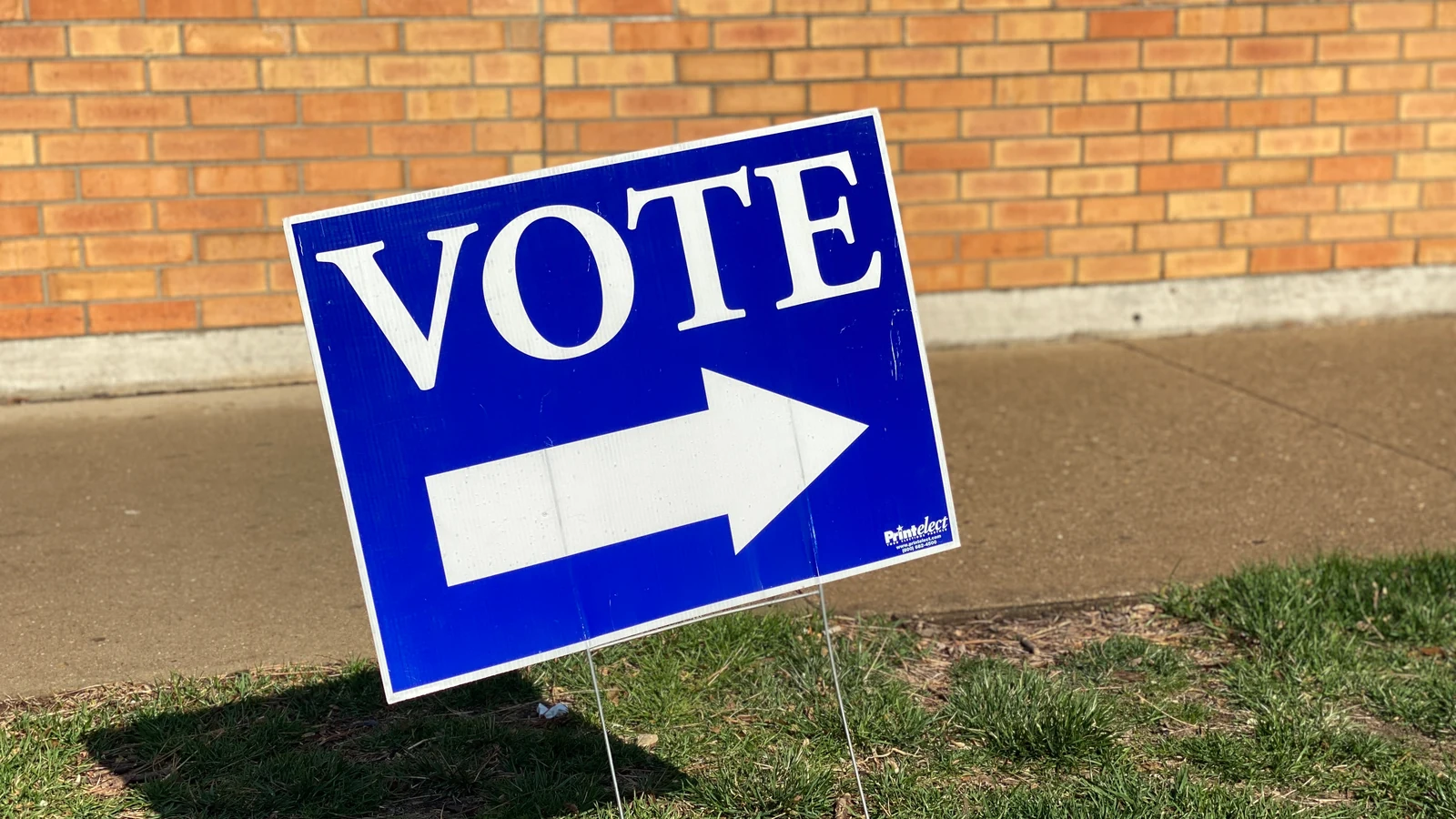A blue Vote sign with an arrow stands beside a sidewalk in Madison, Wisconsin.