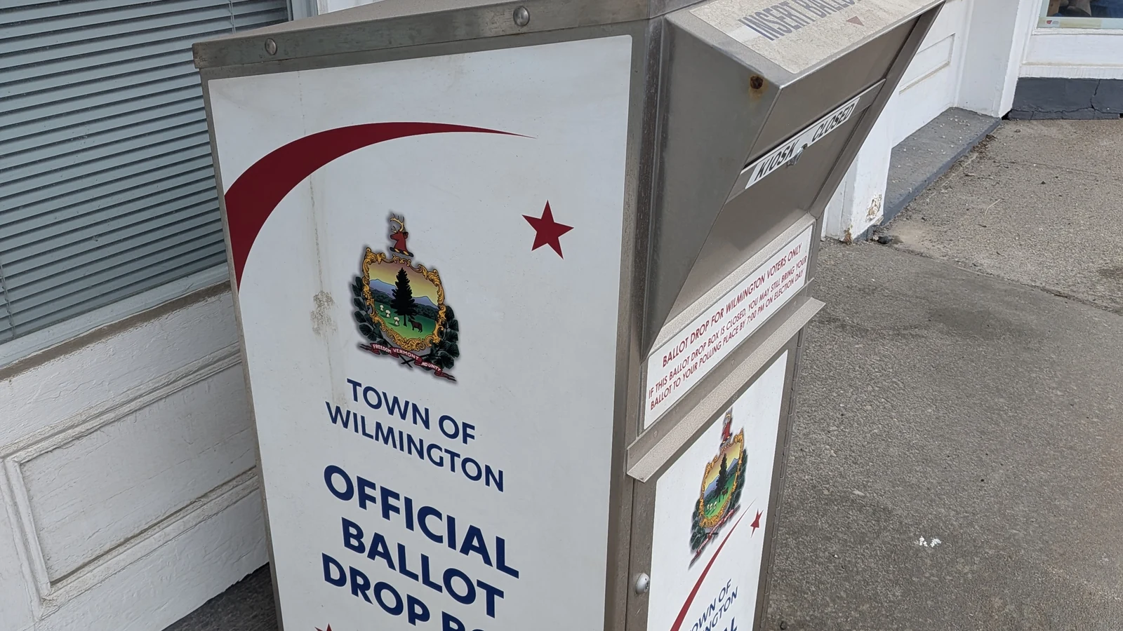 A secured official ballot box stands outside a brick municipal building in Wilmington, Vermont.
