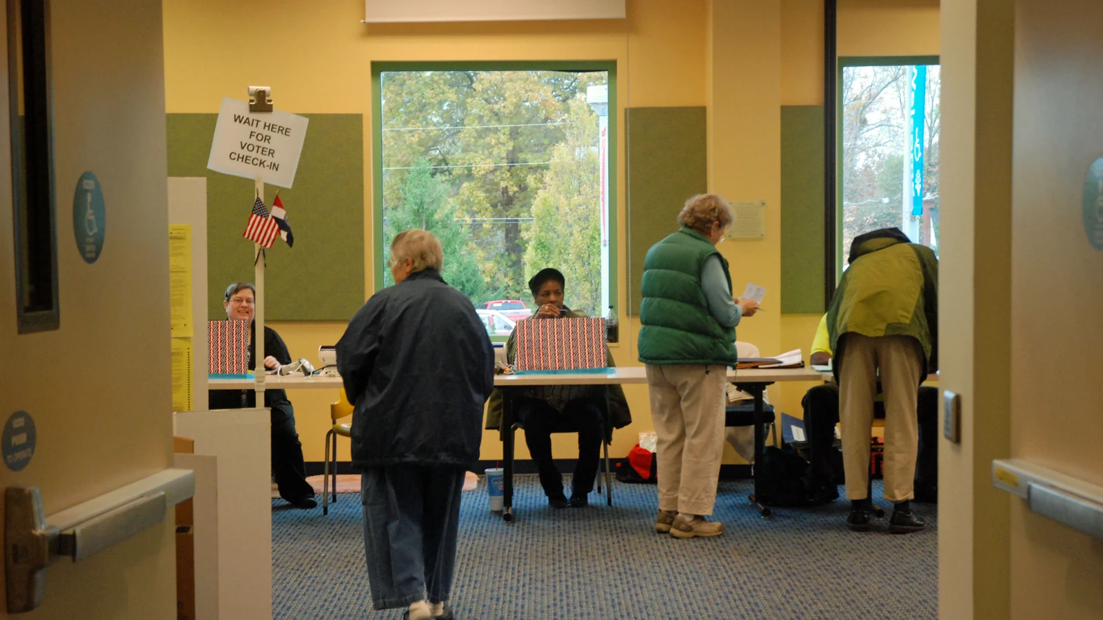 Voters wait in line at a check-in table inside a public library polling place.