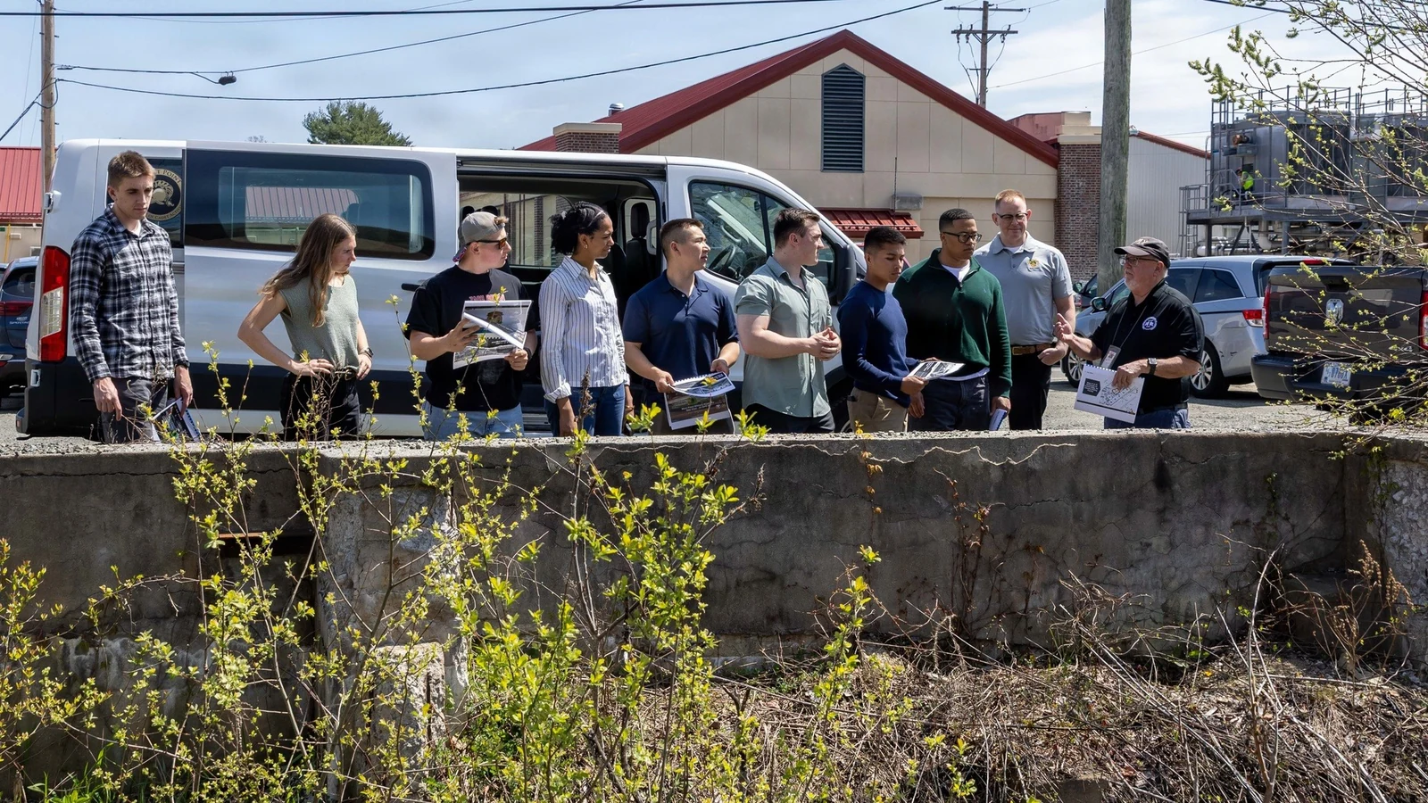 Cadets wearing hard hats stand with an environmental specialist beside a Superfund cleanup area.