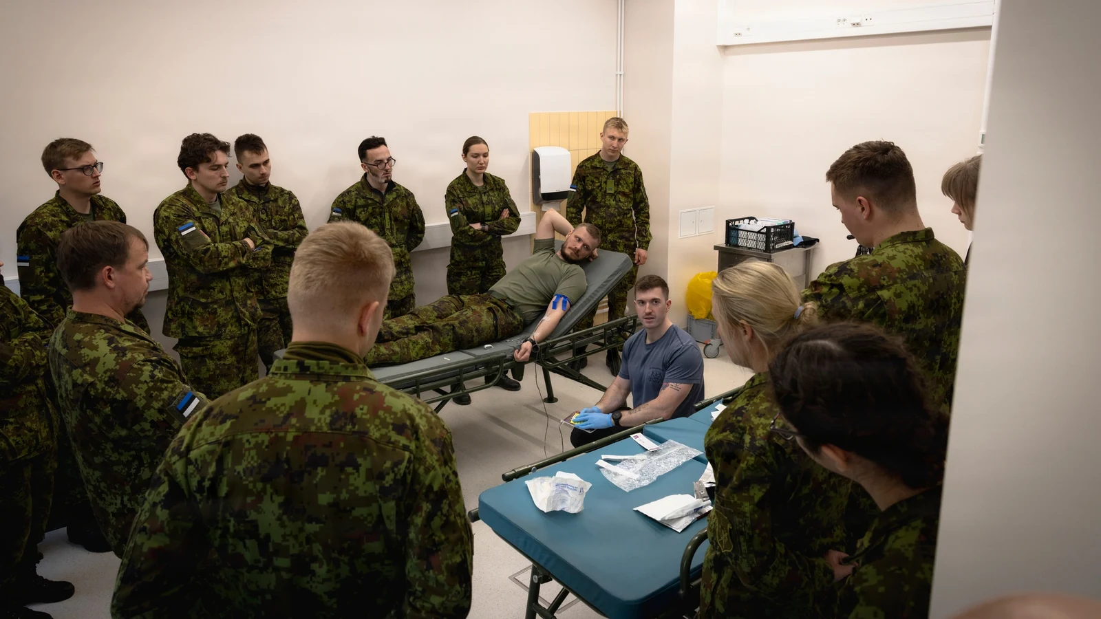 Military medical personnel gather around a patient during hands-on field blood-transfusion training.