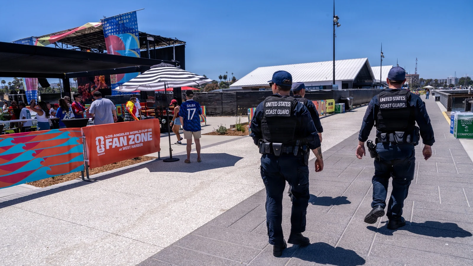 Coast Guard personnel walk past soccer supporters and a World Cup 2026 fan-zone sign on the Los Angeles waterfront.