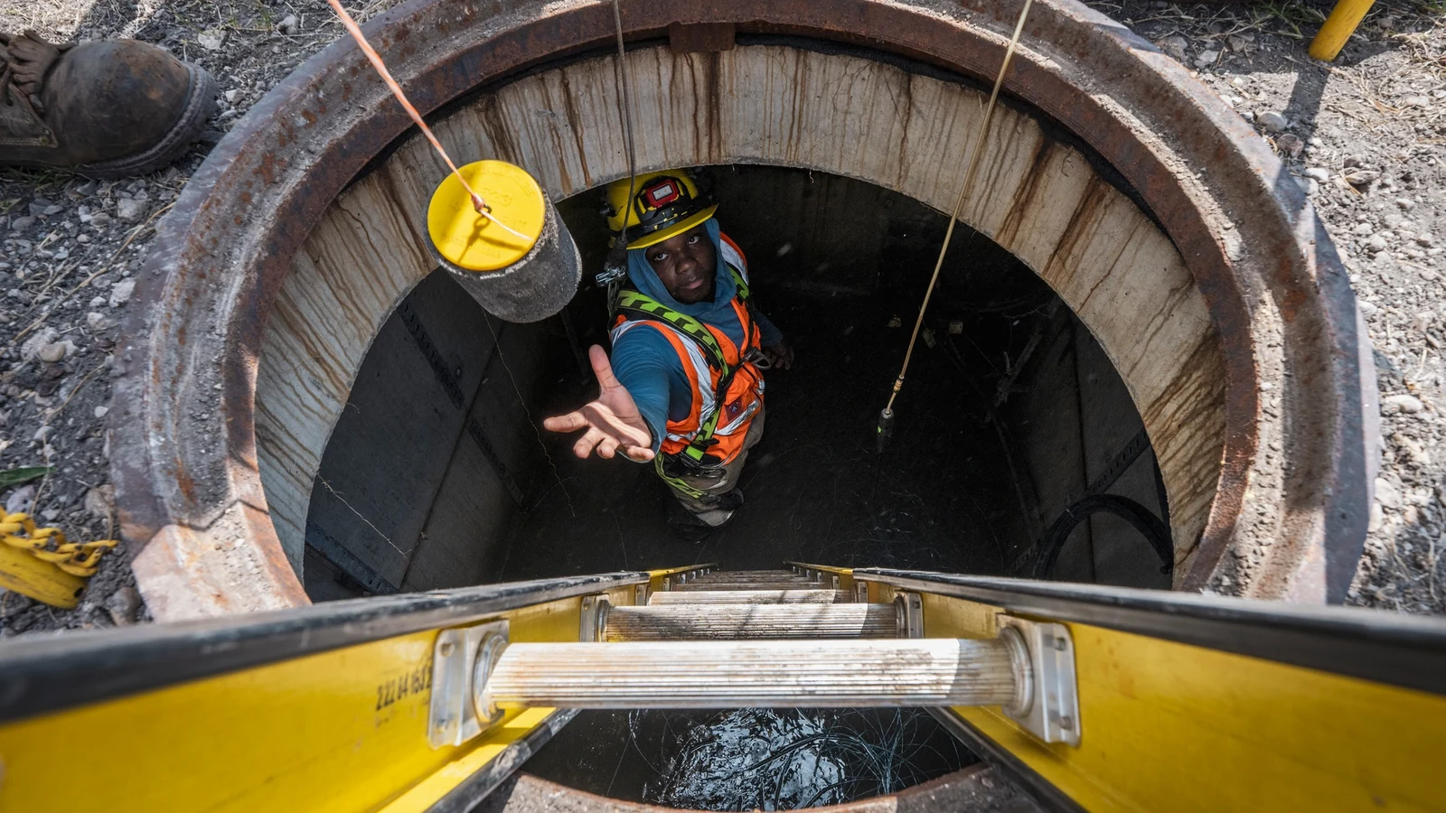 A technician in a utility hole reaches for equipment during underground fiber-optic cable installation.