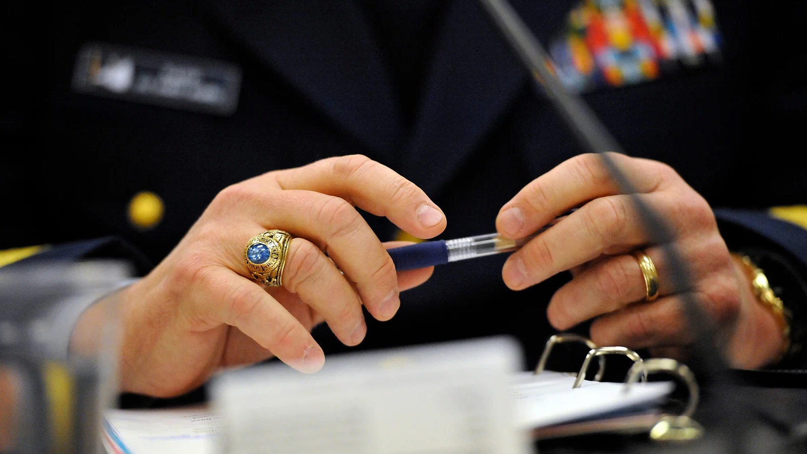 A federal official holds a pen over a binder during a congressional budget hearing.