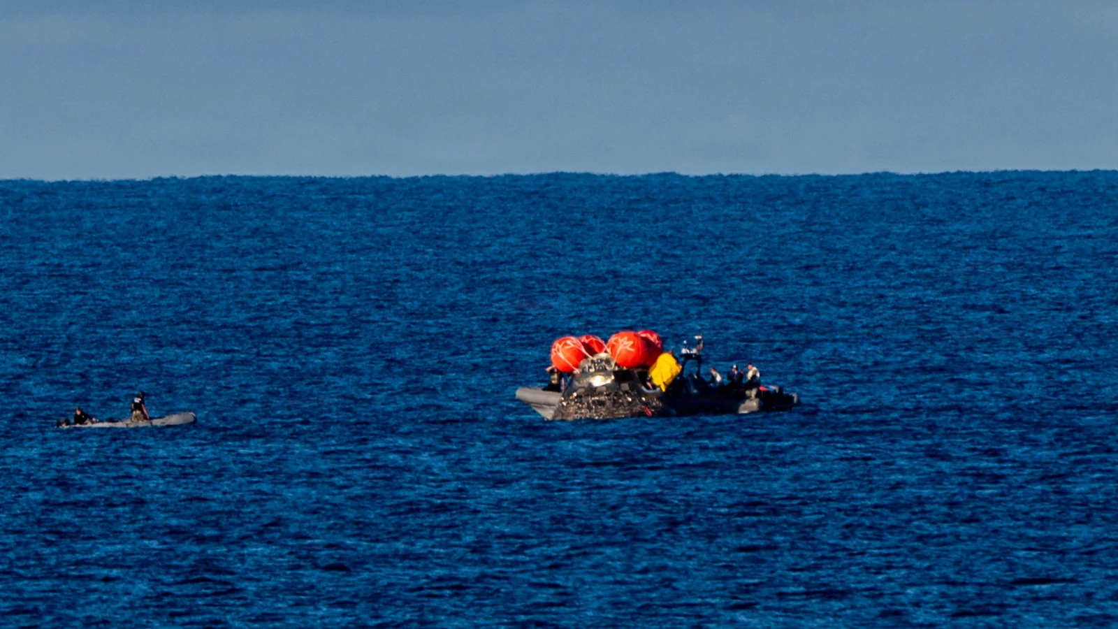 The Orion capsule floats in the Pacific with recovery boats alongside it after the Artemis II mission.