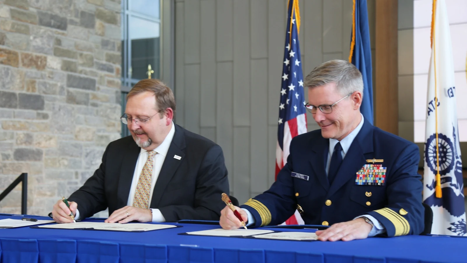 U.S. Coast Guard and USAID officials sit at a table signing an interagency agreement.