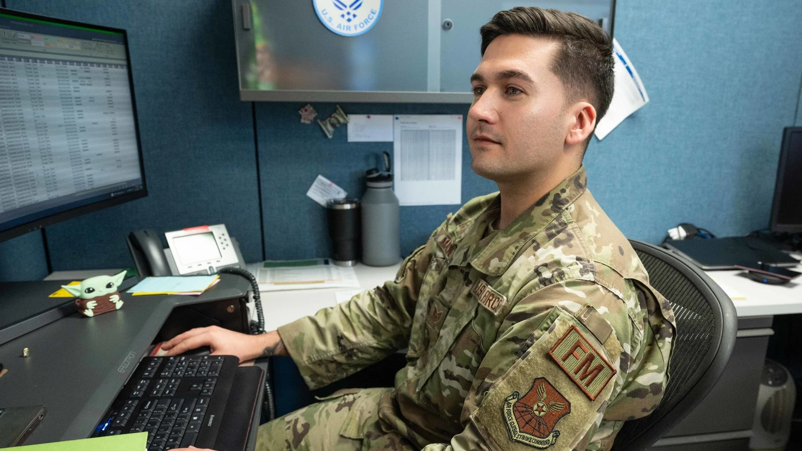 A budget analyst reviews documents at a desk with two computer monitors.