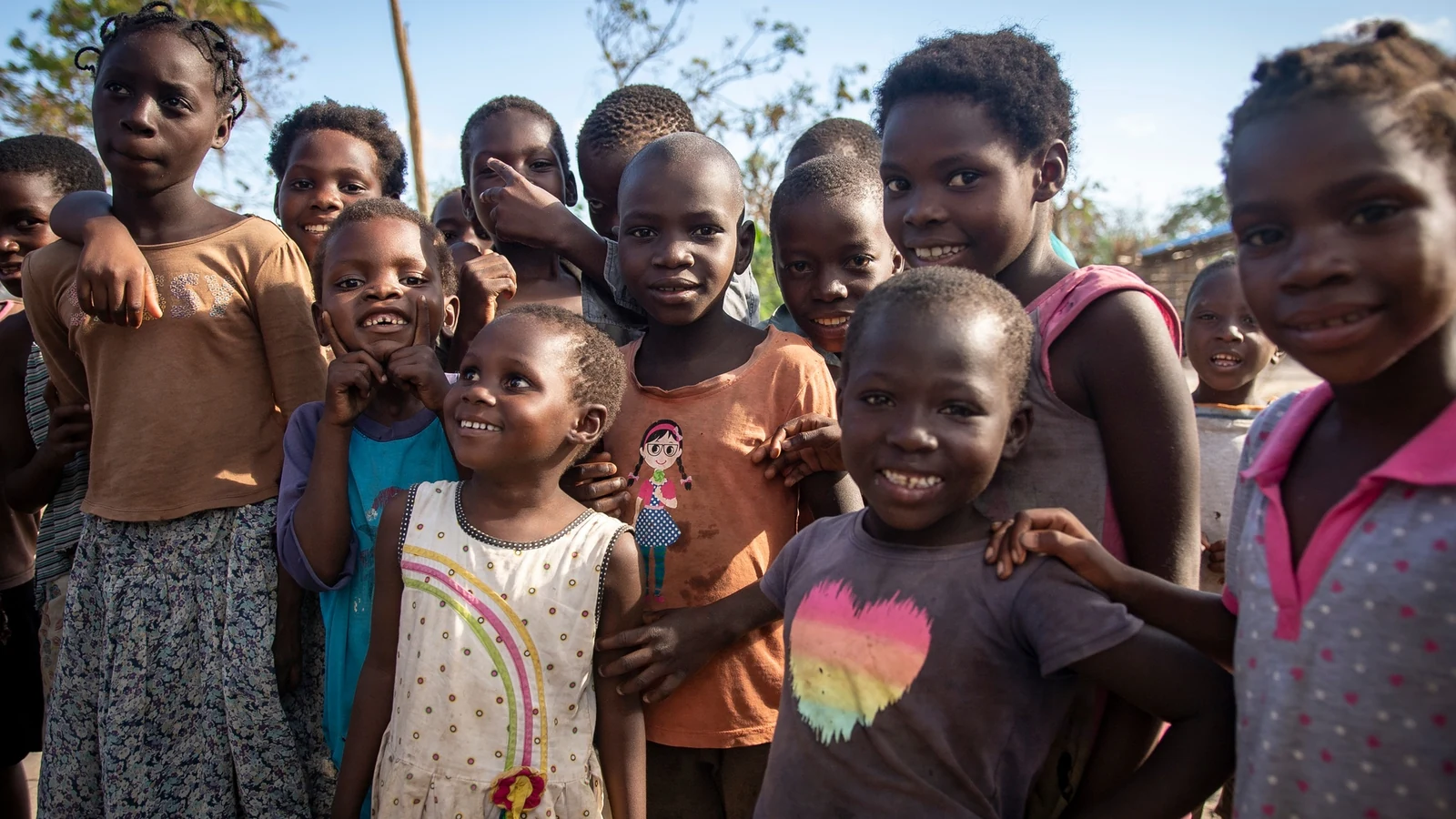 Families wait near stacked food aid during a distribution operation in Mozambique.