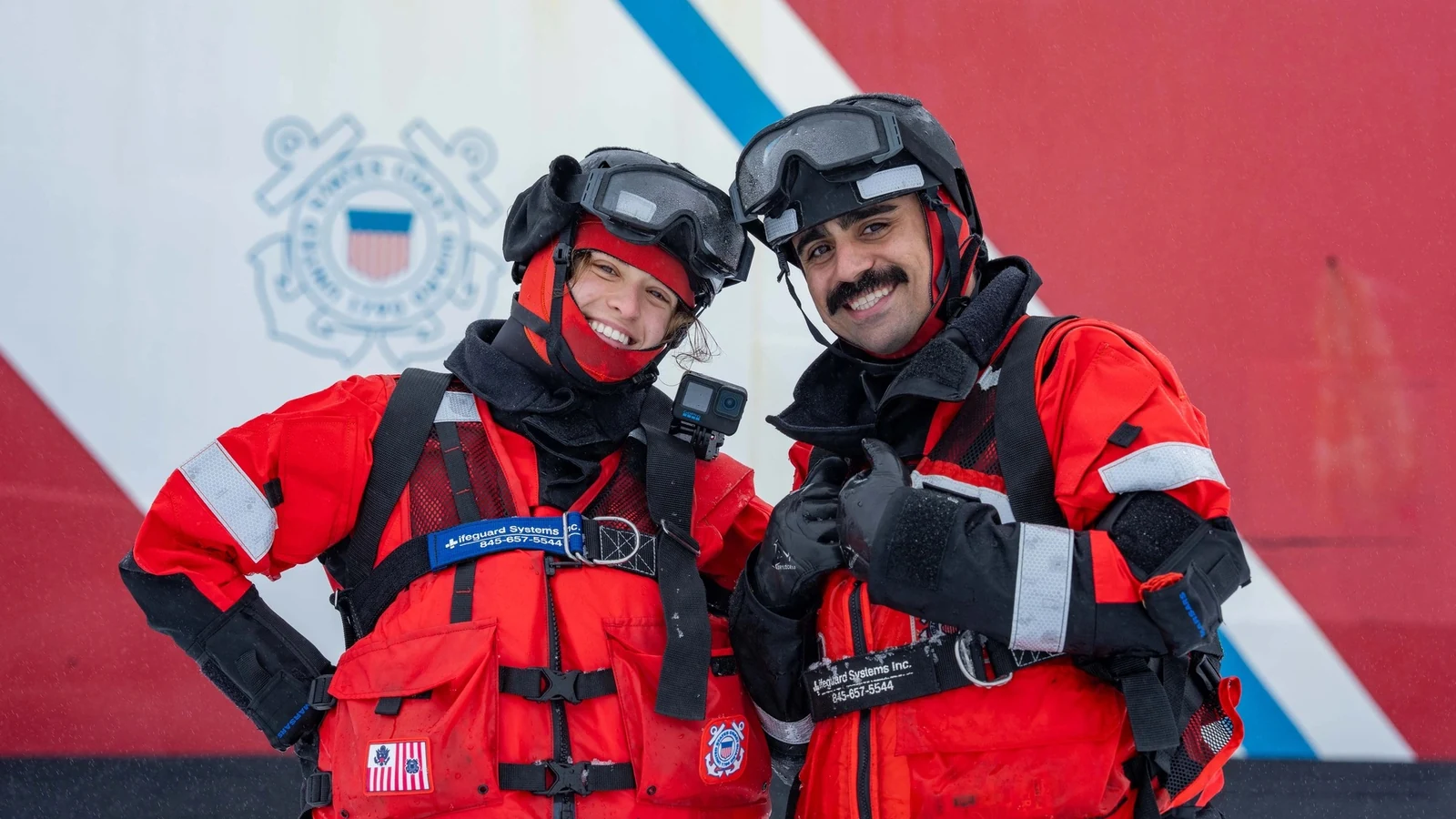 A NOAA Corps officer and a Coast Guard member in red cold-weather gear stand together on Arctic ice in front of an icebreaker.