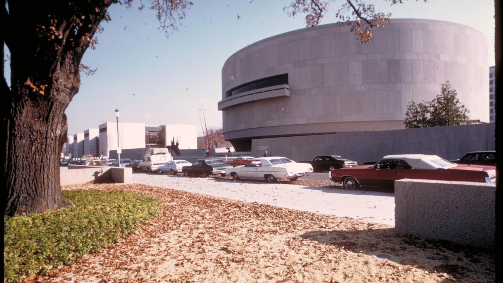 The cylindrical Hirshhorn Museum rises behind trees and parked cars on the National Mall.