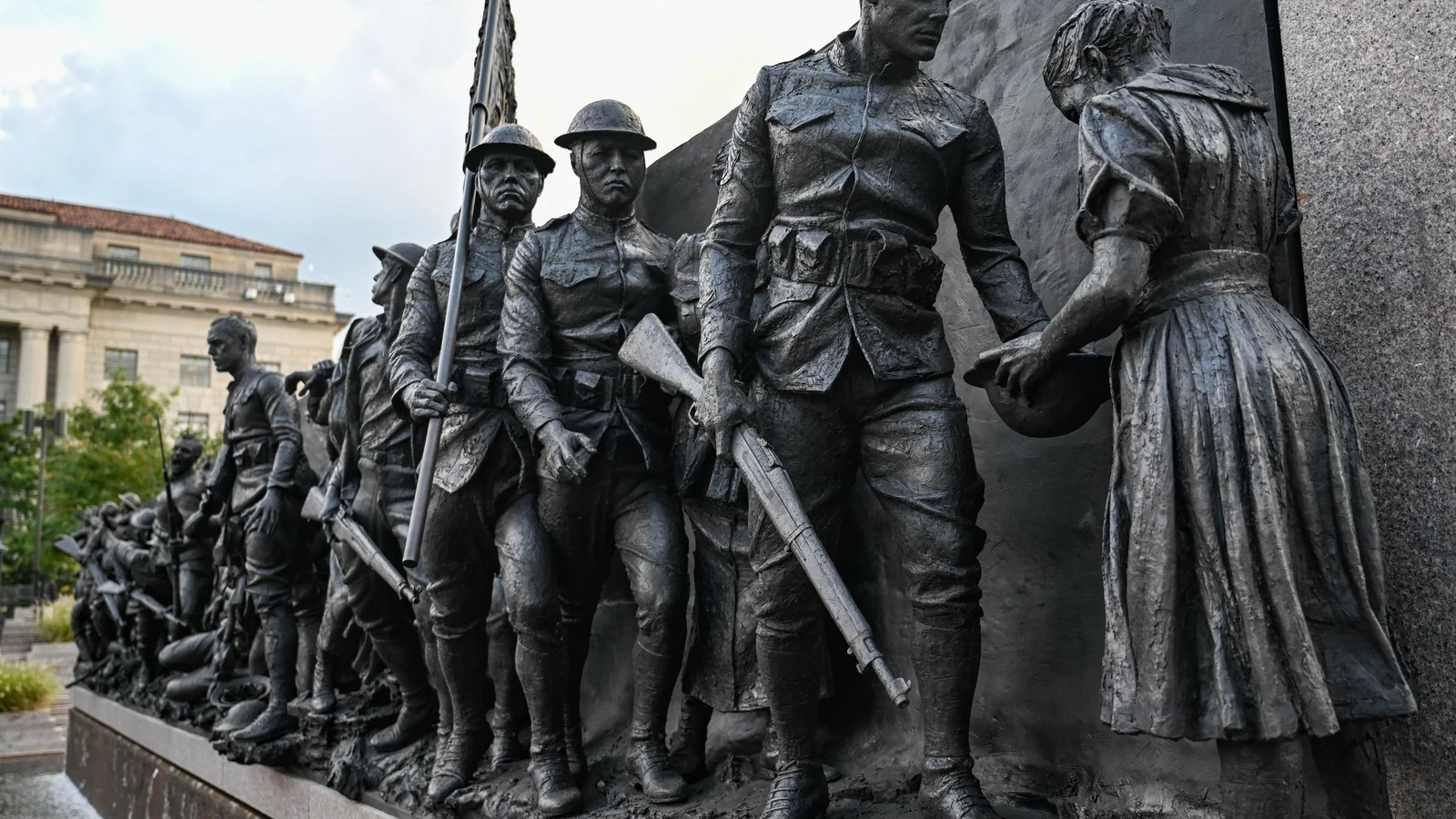 Visitors stand before a long bronze sculpture at an outdoor Washington memorial.
