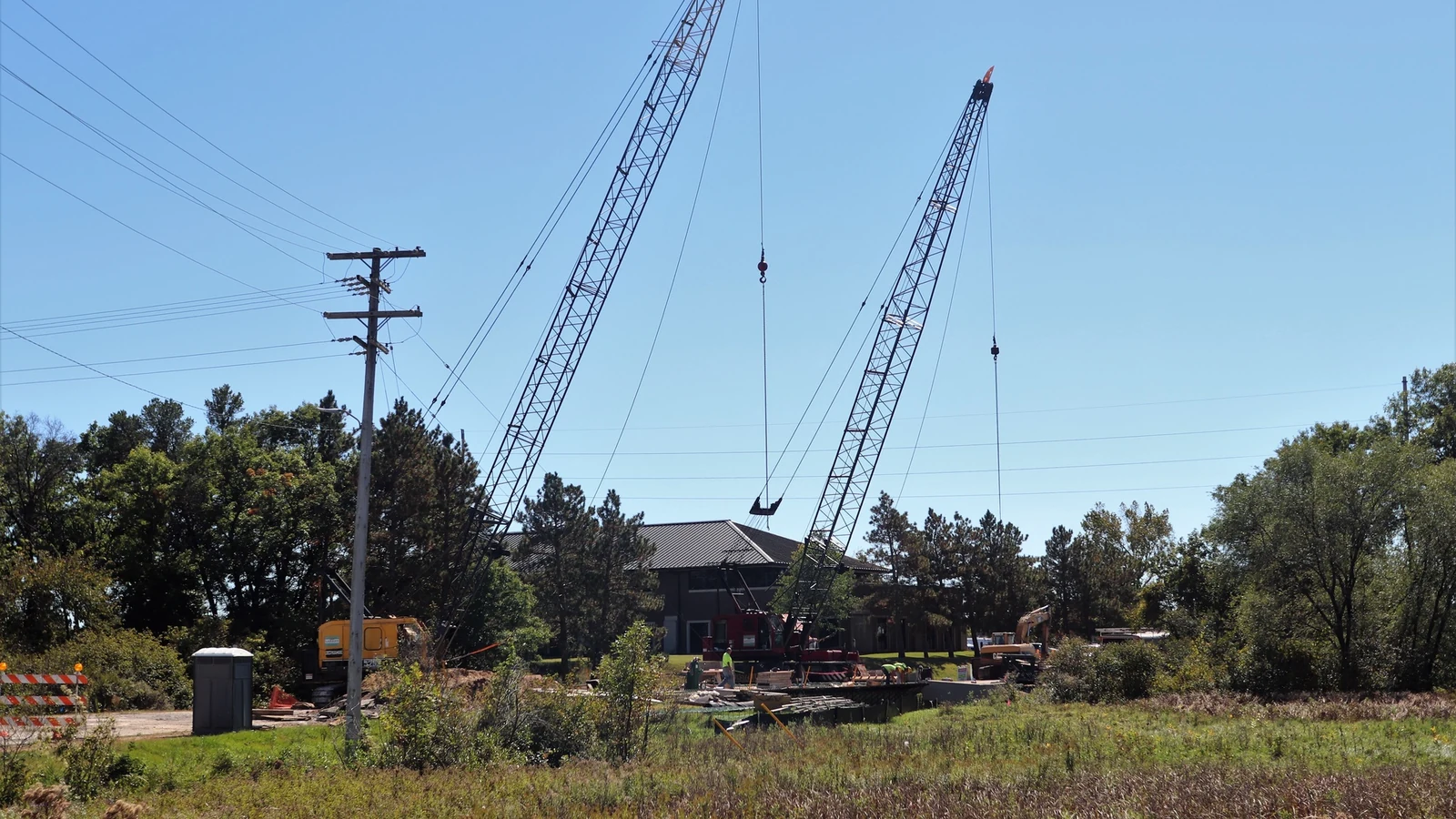 Construction equipment and workers build a bridge over a roadway.
