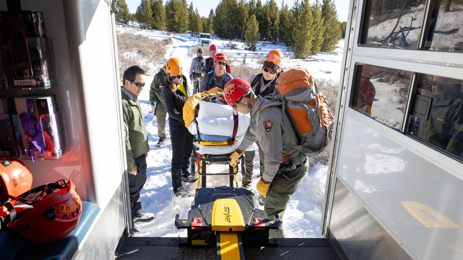 Rescue trainees load a patient on a wheeled stretcher into an ambulance during a field exercise.