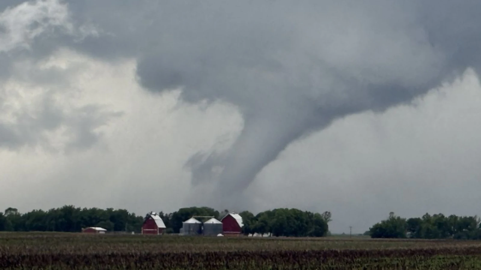 A tornado descends from a dark storm cloud beyond farm buildings near Streator, Illinois.