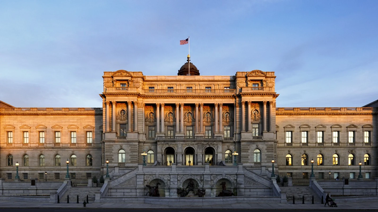 The illuminated Thomas Jefferson Building of the Library of Congress stretches across the frame at dusk.