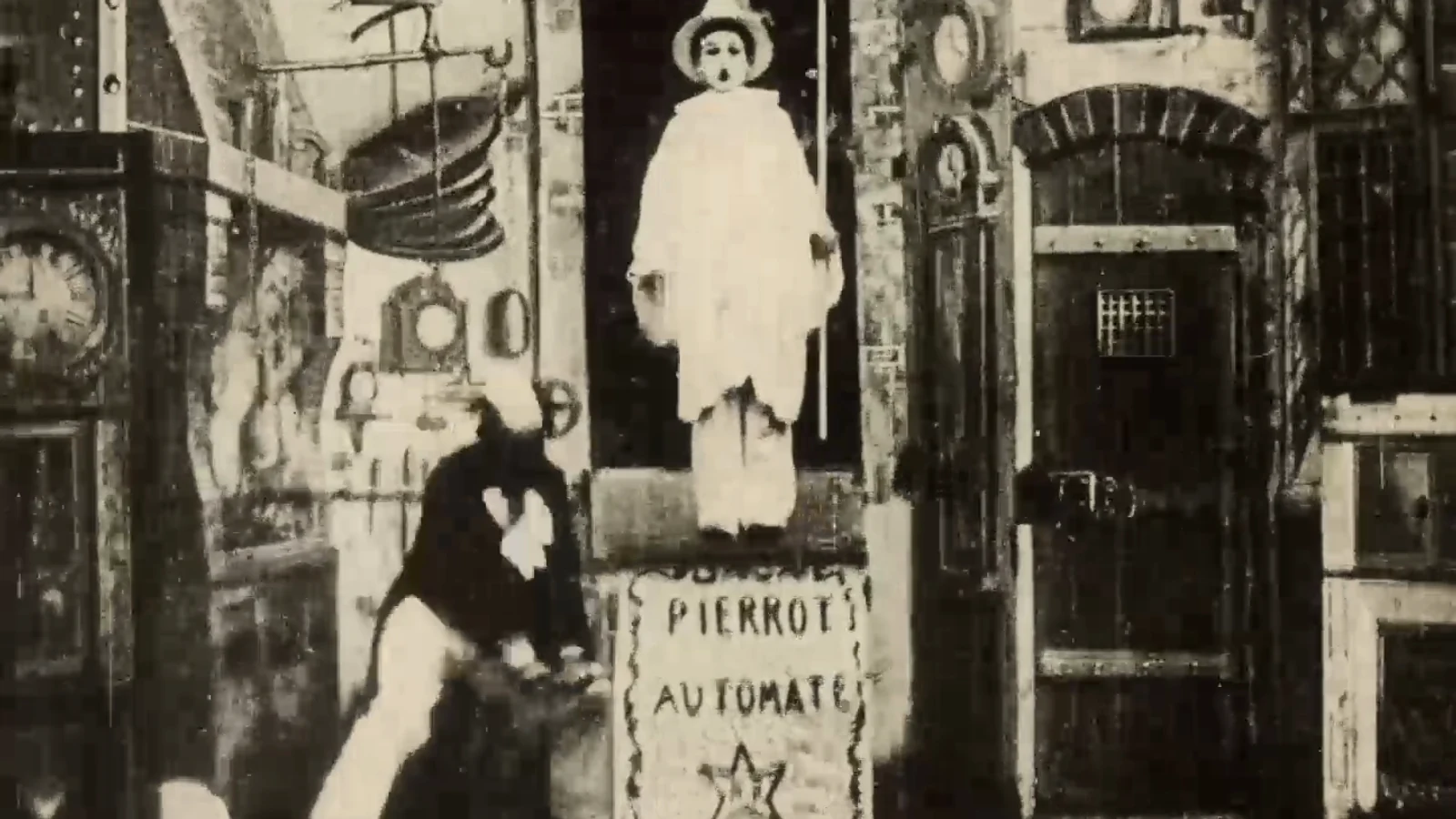 A black-and-white frame shows the white-costumed Pierrot automaton standing over Georges Méliès in a painted workshop set.