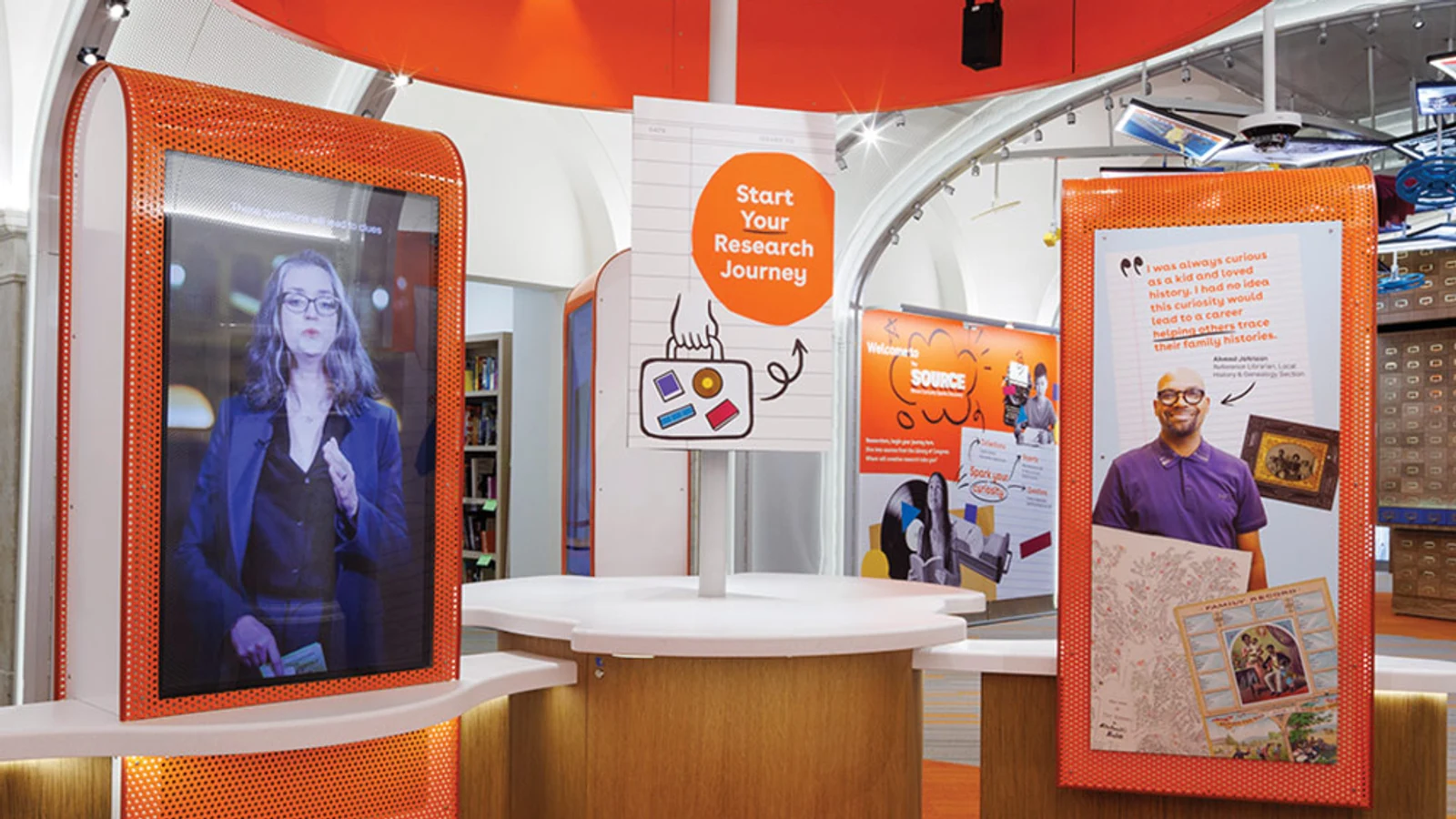 An orange-and-white interactive research kiosk with large video displays inside The Source at the Library of Congress.