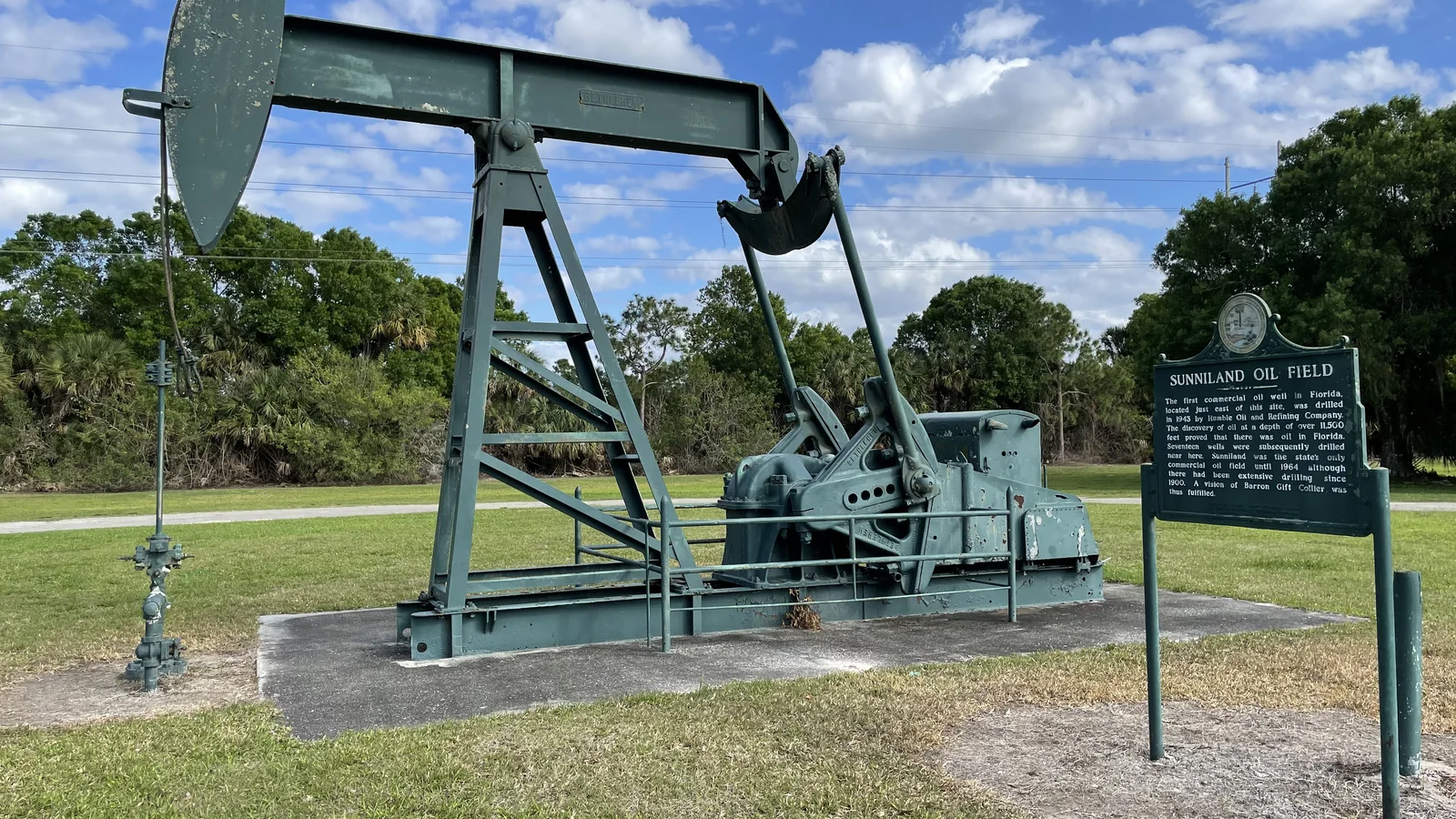 Preserved black pumpjack stands beside a roadway under a bright sky.