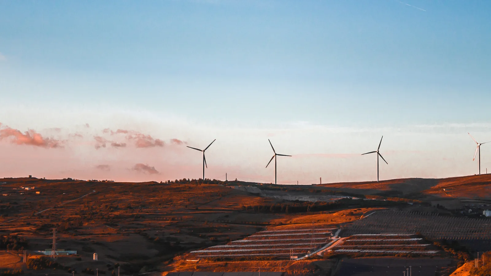 Wind turbines stretch across a green mountain ridge beneath cloudy sky.