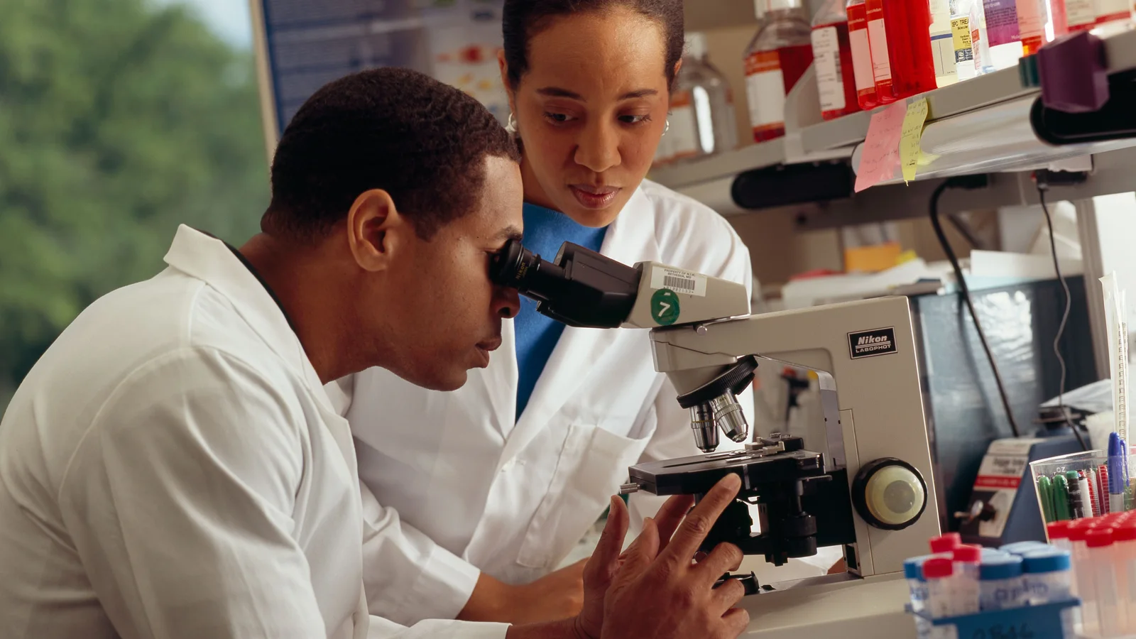 Laboratory researcher looks through a microscope beside scientific equipment.