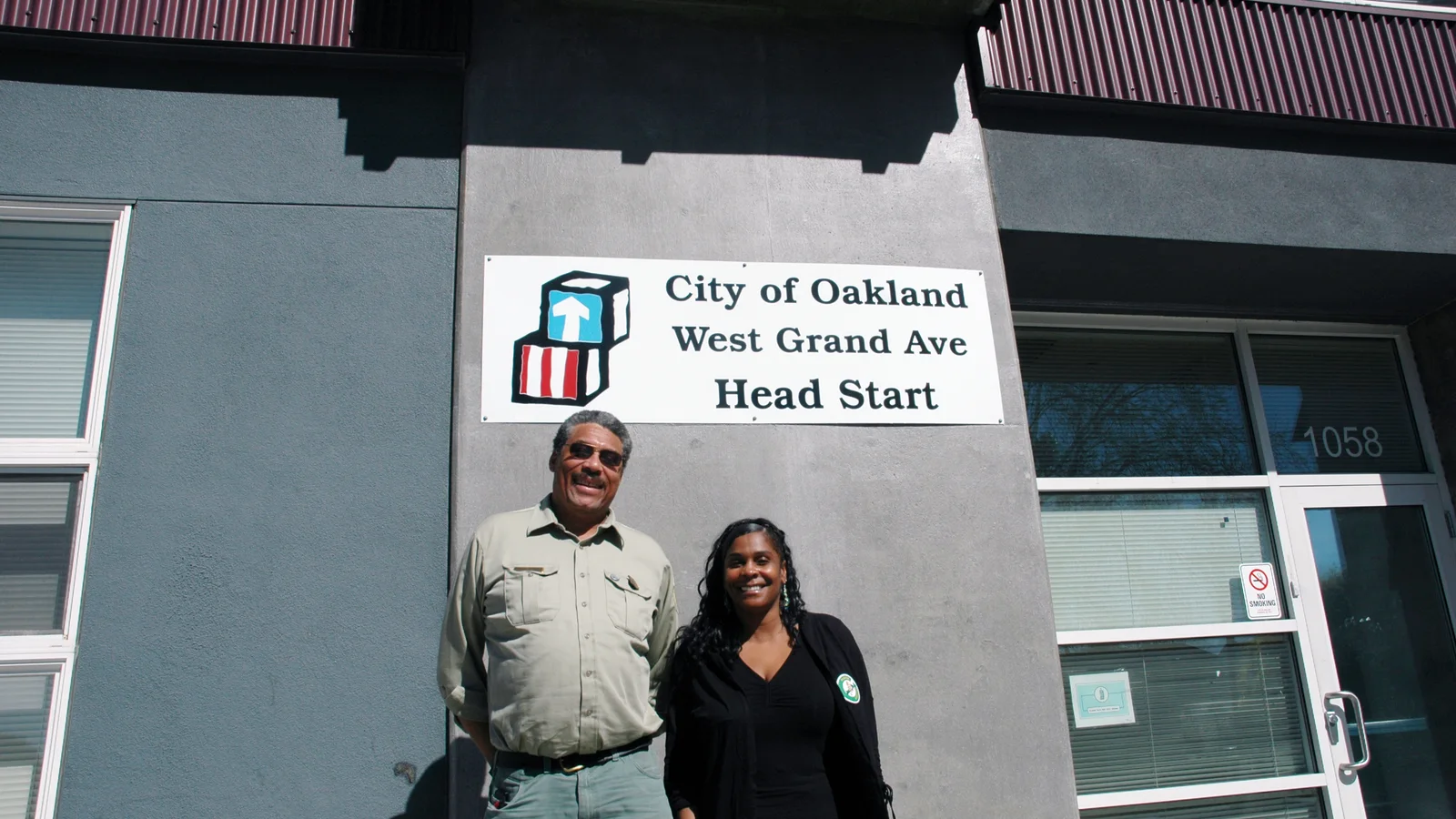 Two adult staff members stand outside a Head Start program building.