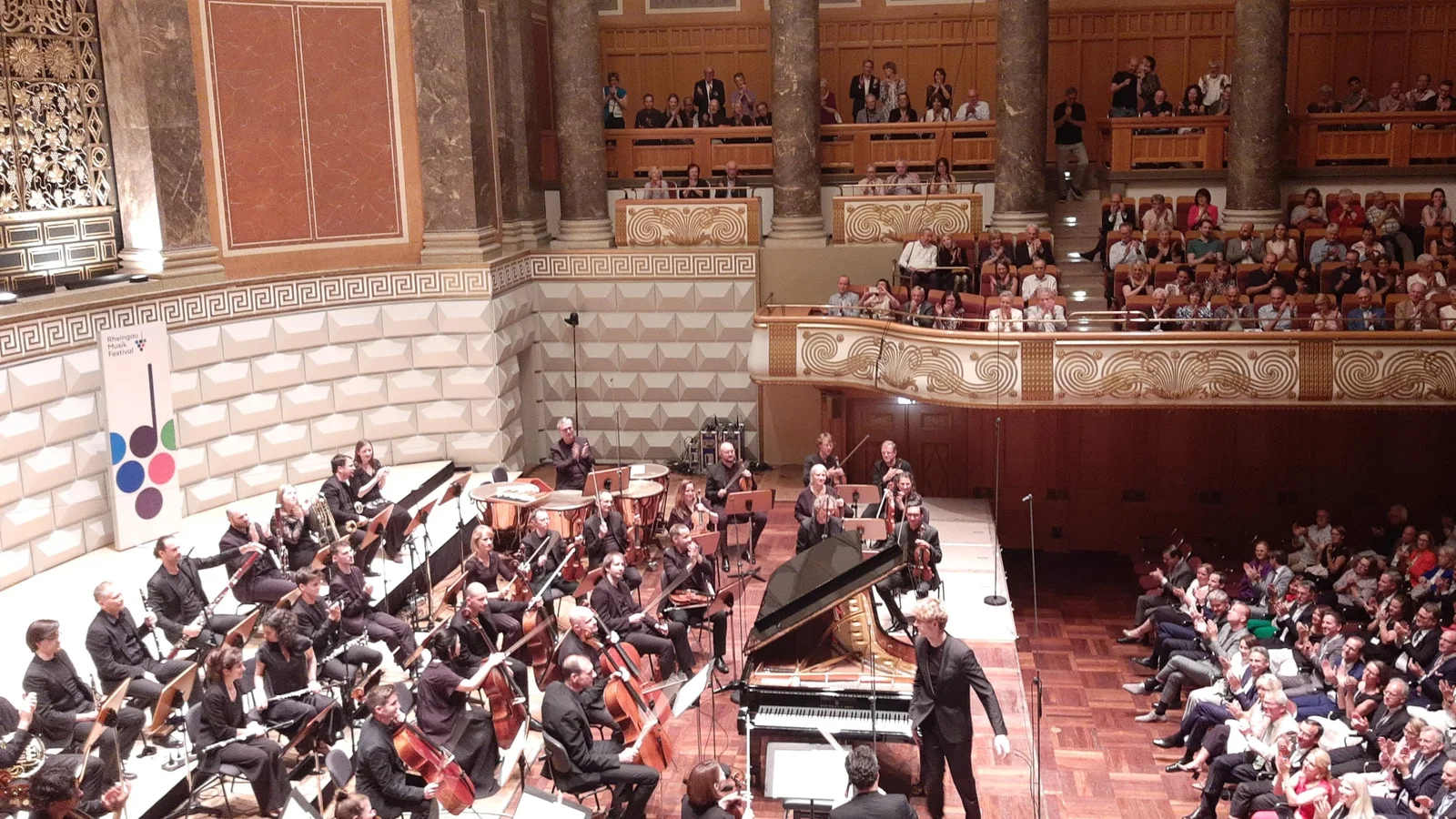 Chamber orchestra and pianist take applause on a concert-hall stage.