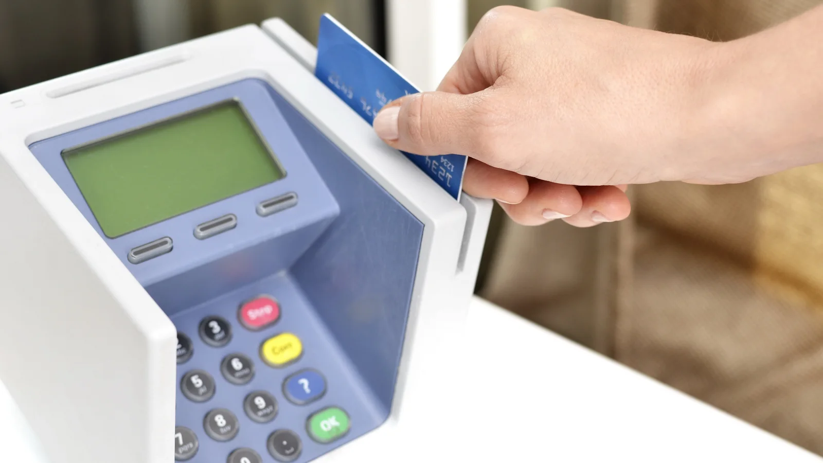 Hand slides a payment card through a blue point-of-sale terminal.