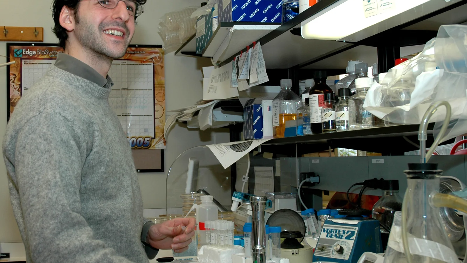 Scientist in a white laboratory coat works at a bench with research equipment.