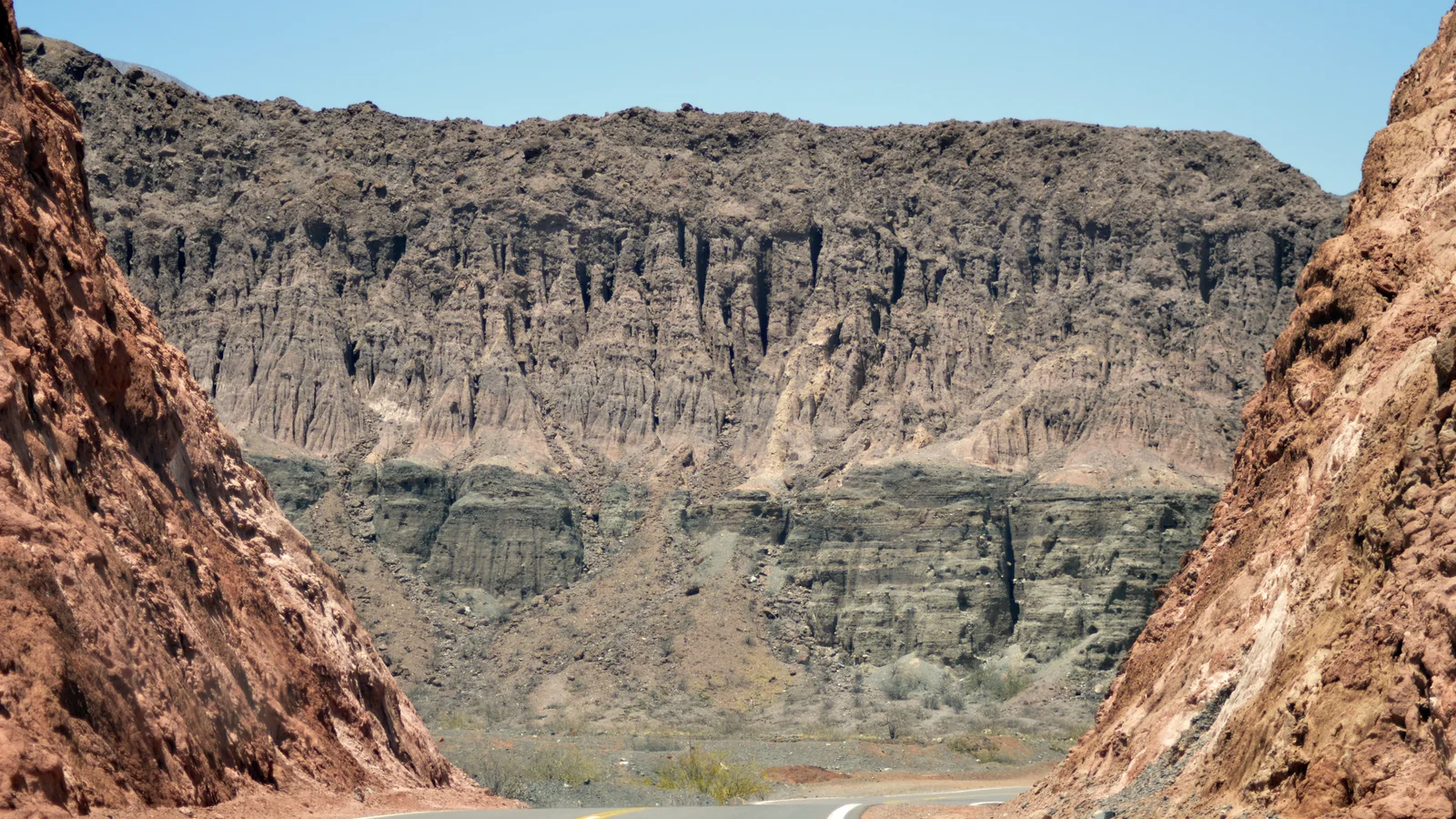 Two-lane road curves through dry mountains under a blue sky in Salta Province.