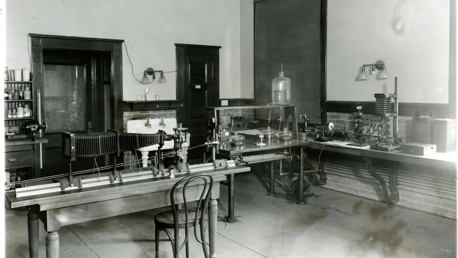 A large historic metallurgy laboratory contains optical instruments, glassware and testing equipment on long benches.