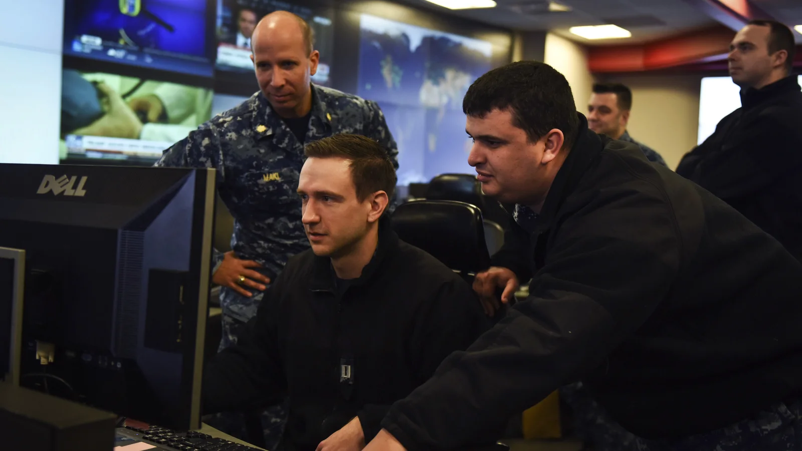 Analysts work at computer stations beneath large information displays in a cyber operations center.