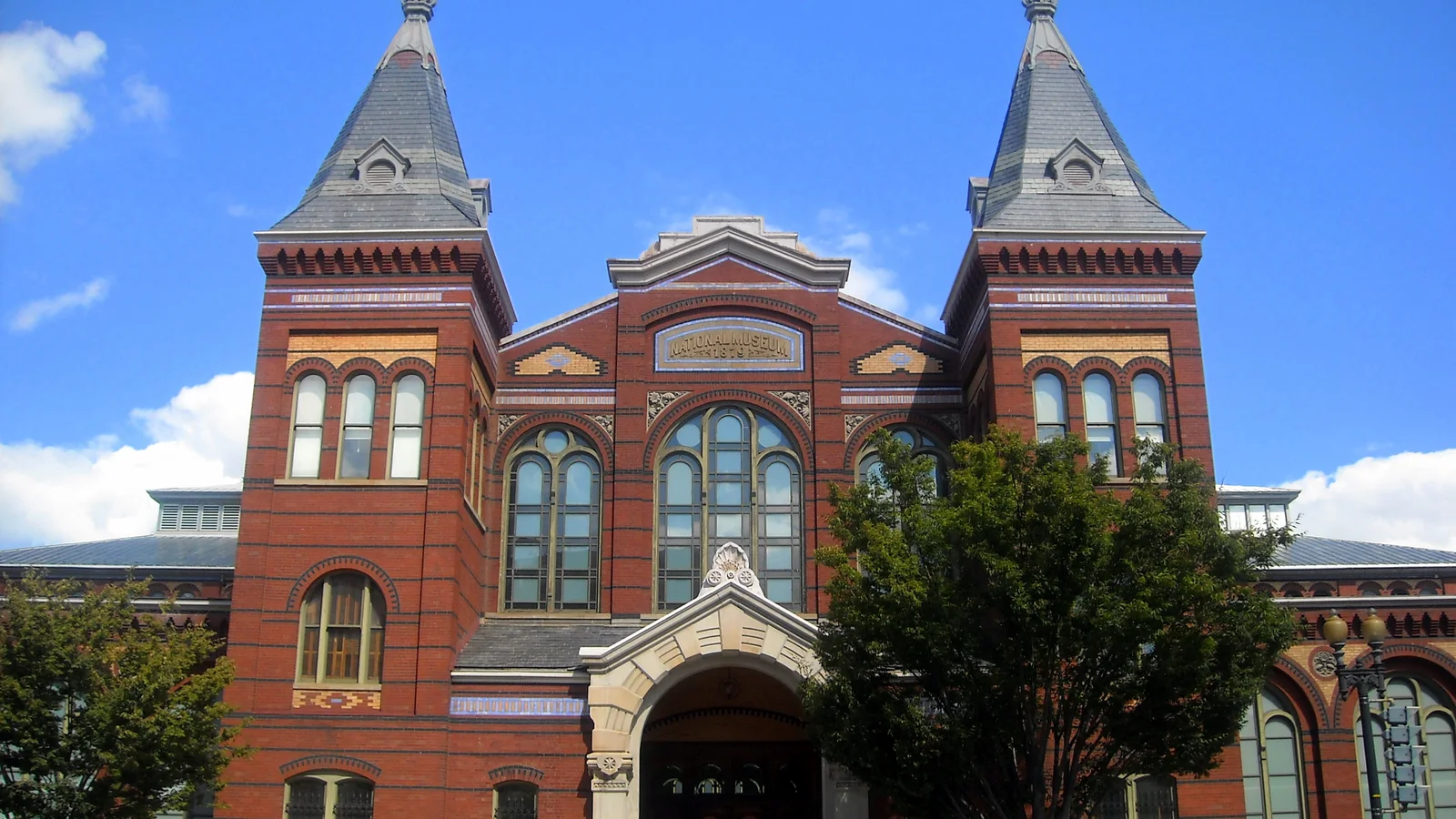 The red-brick and stone Smithsonian Arts and Industries Building stands behind trees and a broad lawn.