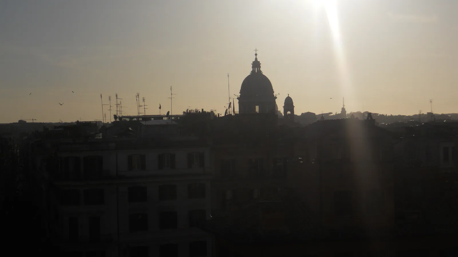 Rome skyline with domes, tiled roofs and distant hills under a blue sky.
