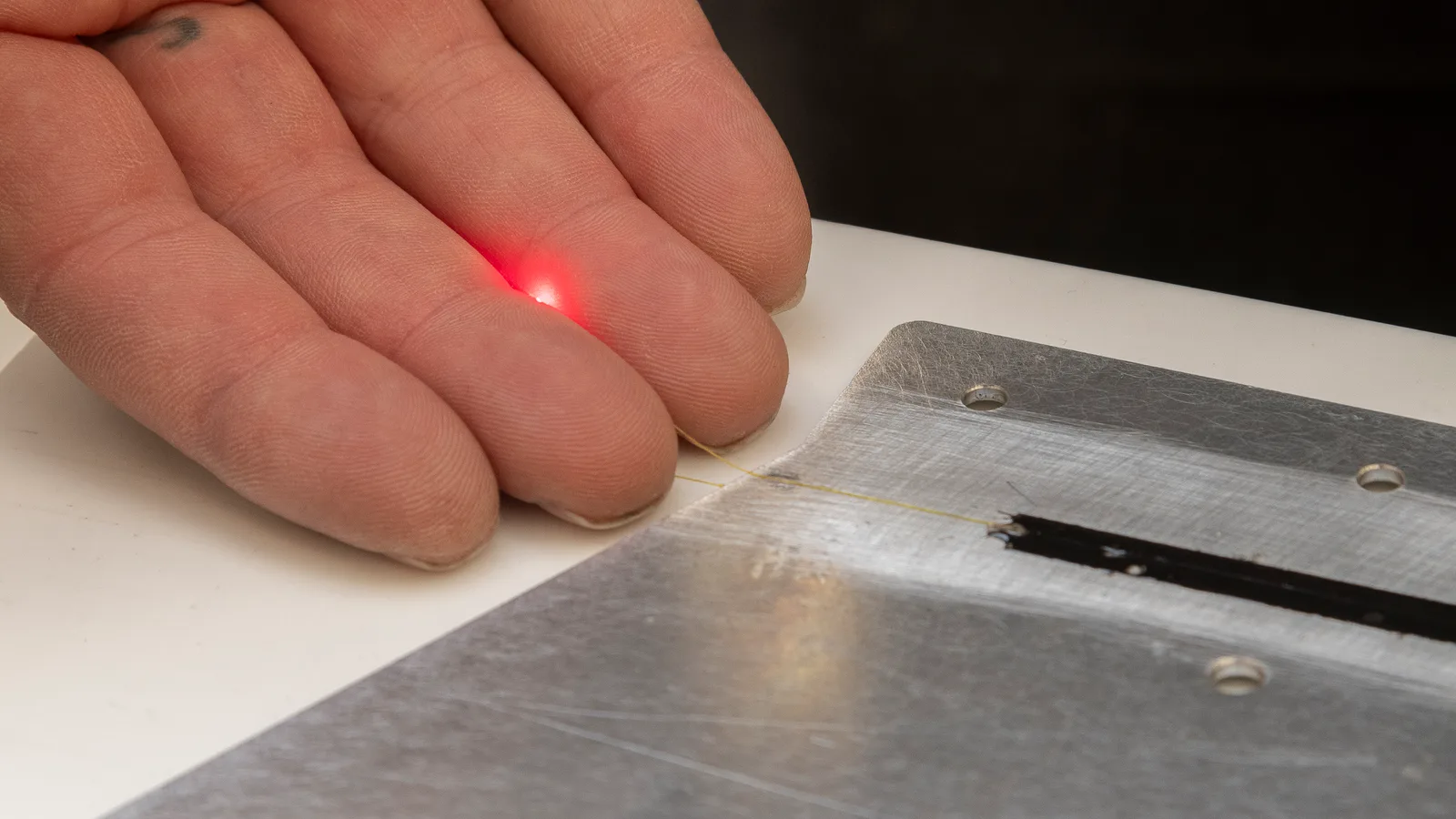 A technician's hand and a red sensor light above a metal wing-test component.