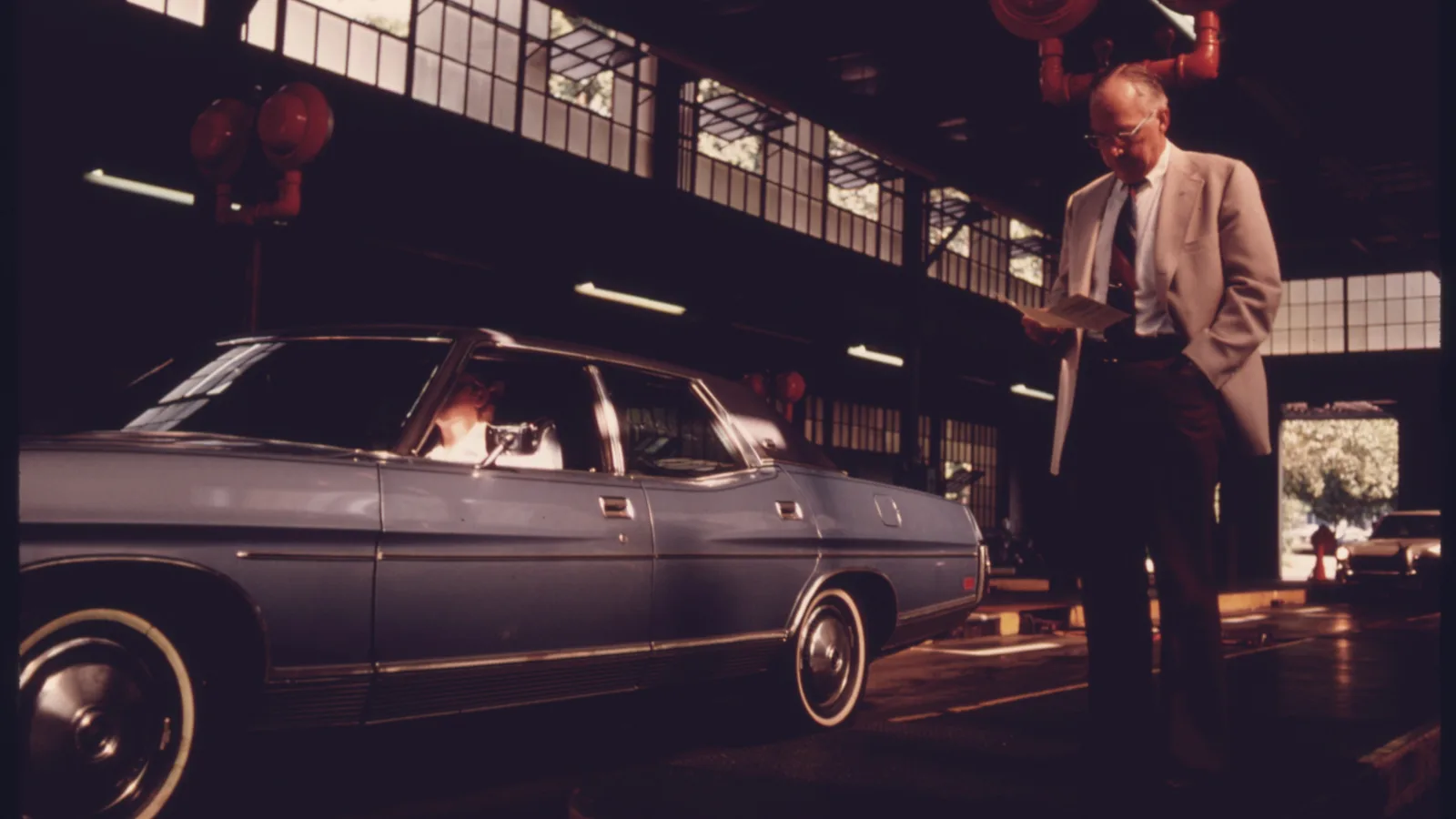 A motorist reads a brochure while a car undergoes an exhaust-emissions test.