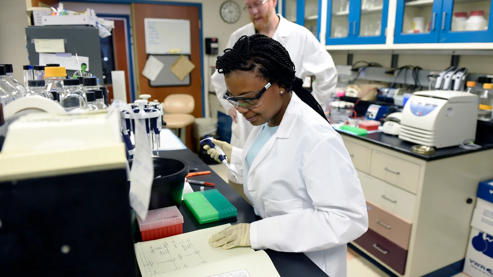 A biomedical engineering student and molecular biologist work with laboratory equipment.