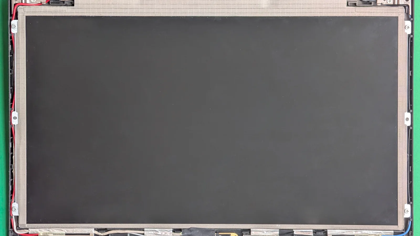A disassembled laptop LCD screen assembly with layers and cables visible.