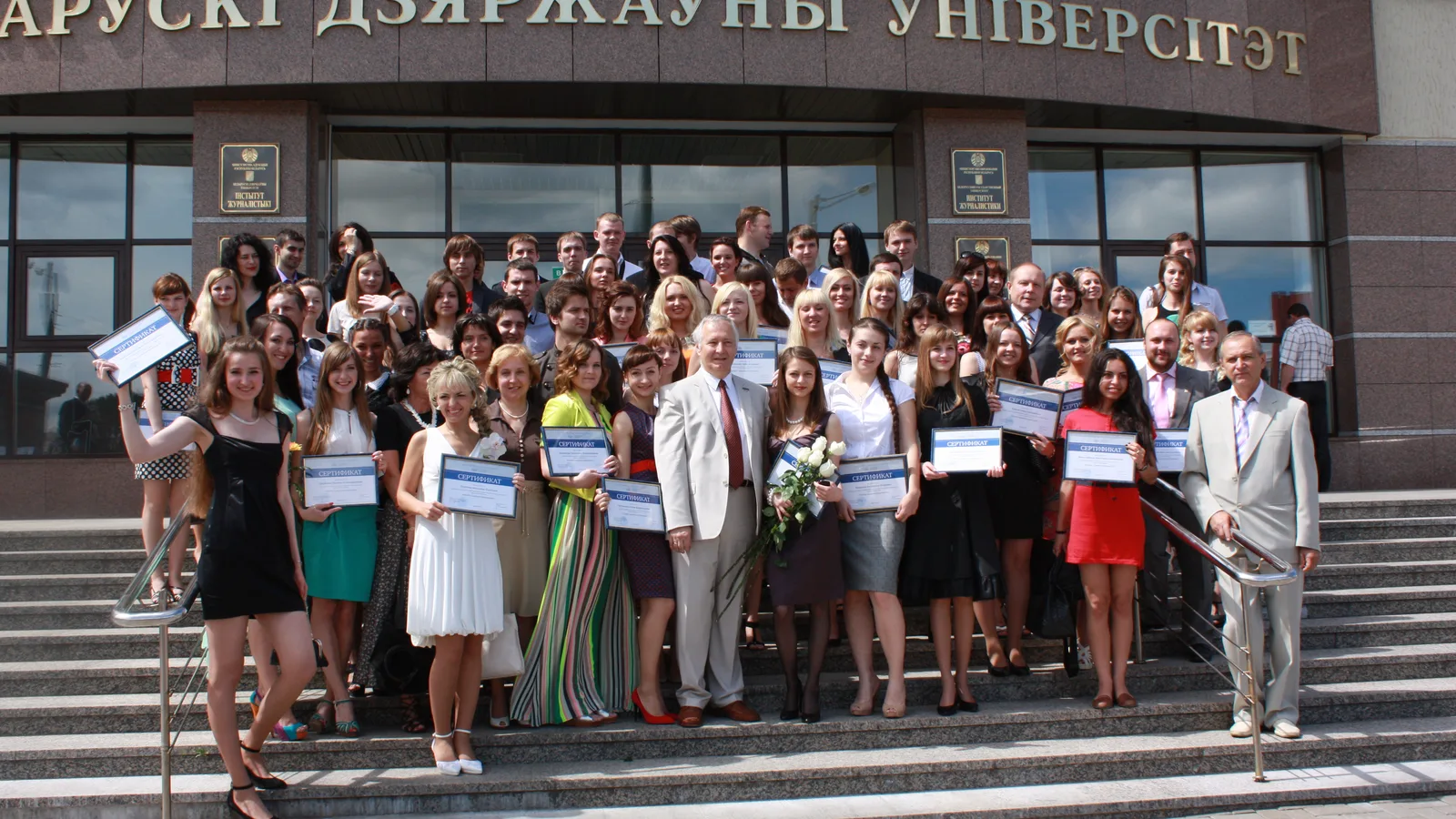 University graduates gathered on the steps outside an academic building.
