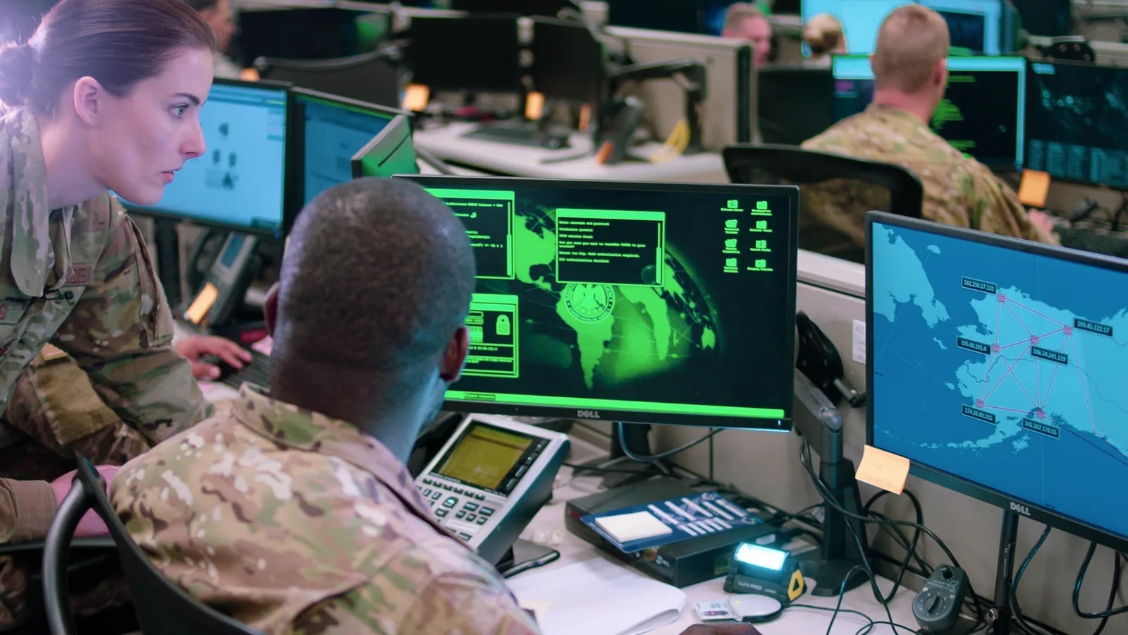 Cybersecurity workers seated at computer stations in a dark operations room.