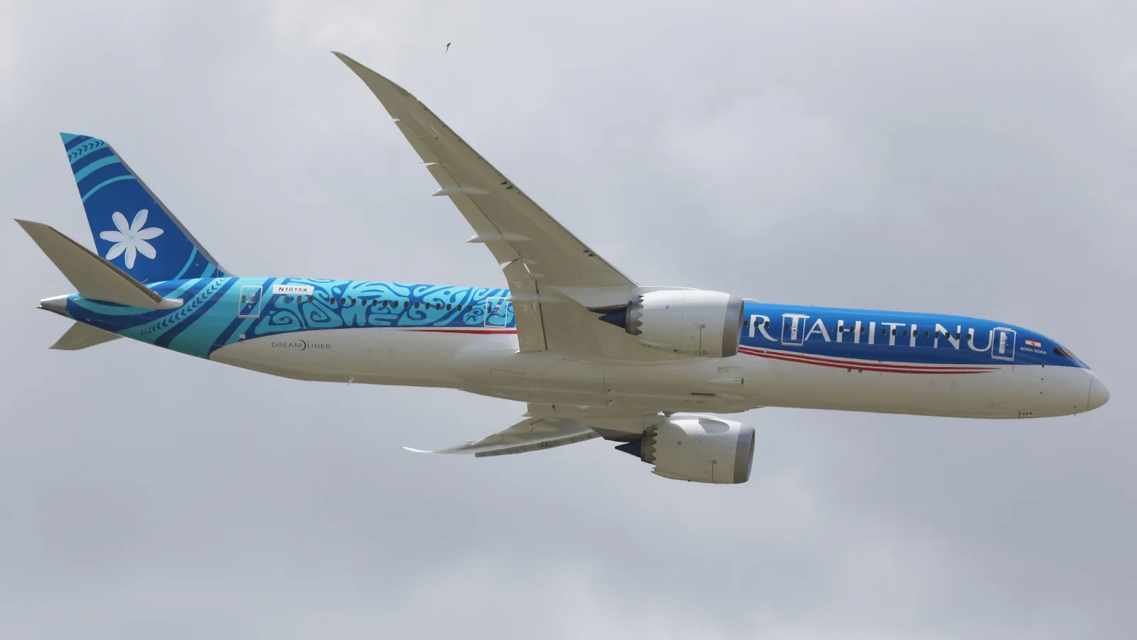 Boeing 787-9 Dreamliner flying against a pale sky.