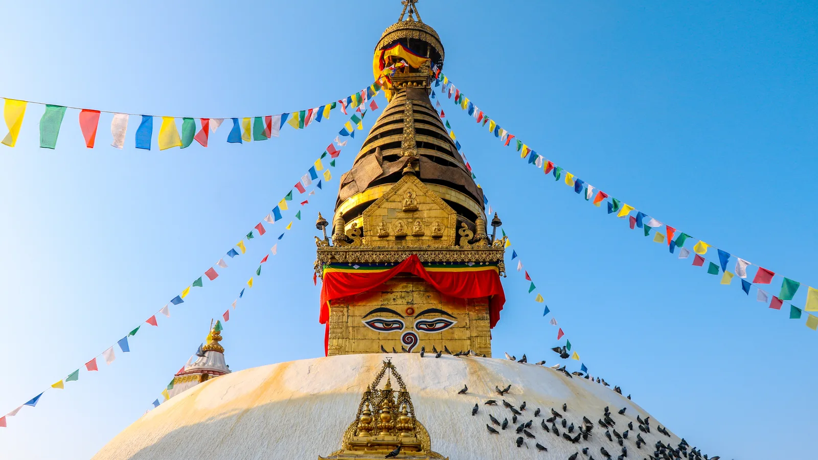 Historic white and gold religious structures at Swayambhunath under a blue sky.