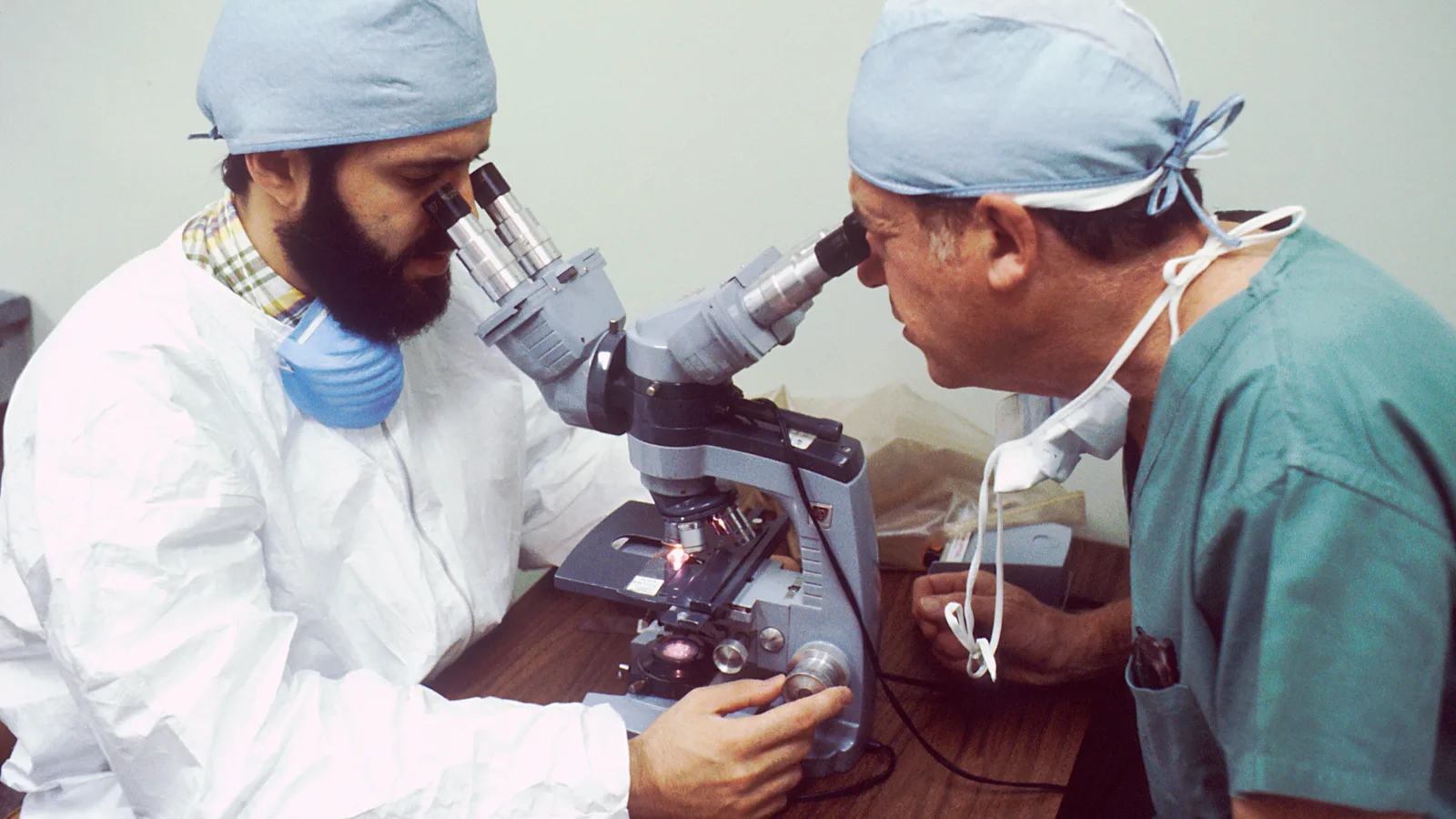 Two pathologists in white laboratory coats looking into microscopes.
