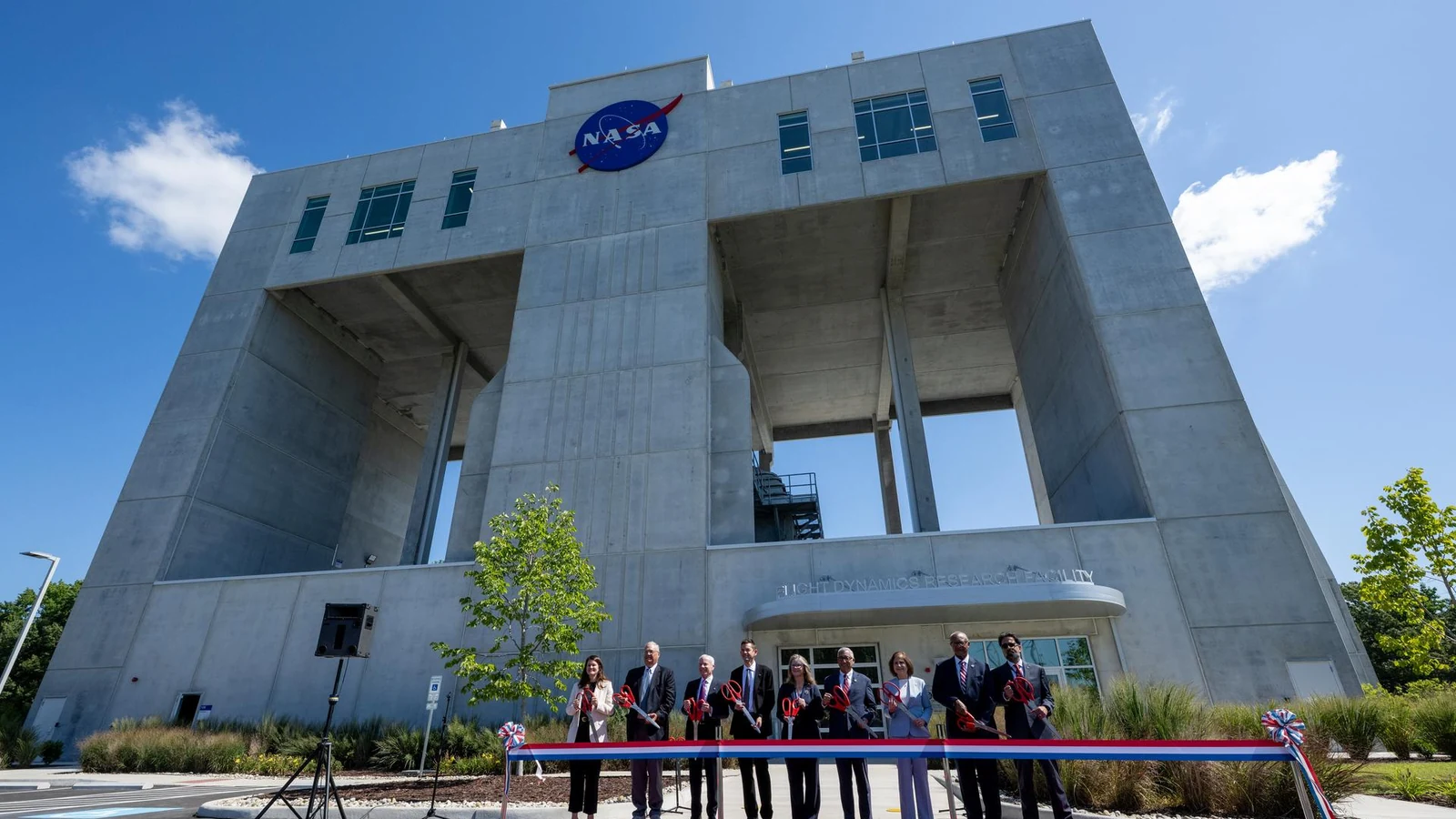 NASA, federal, state and local officials stand outside a new research building before cutting a blue ribbon.