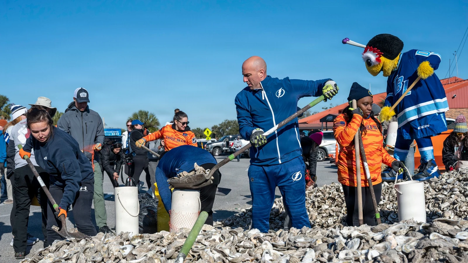 Volunteers build a living shoreline with oyster-shell bags beside coastal water.